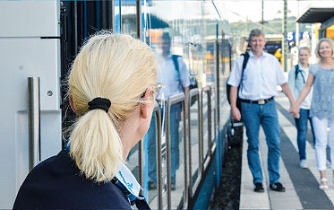 Eine Kundenbetreuerin schaut aus dem Zug einem händchenhaltenden Päärchen entgegen, das auf dem Bahnsteig spaziert.