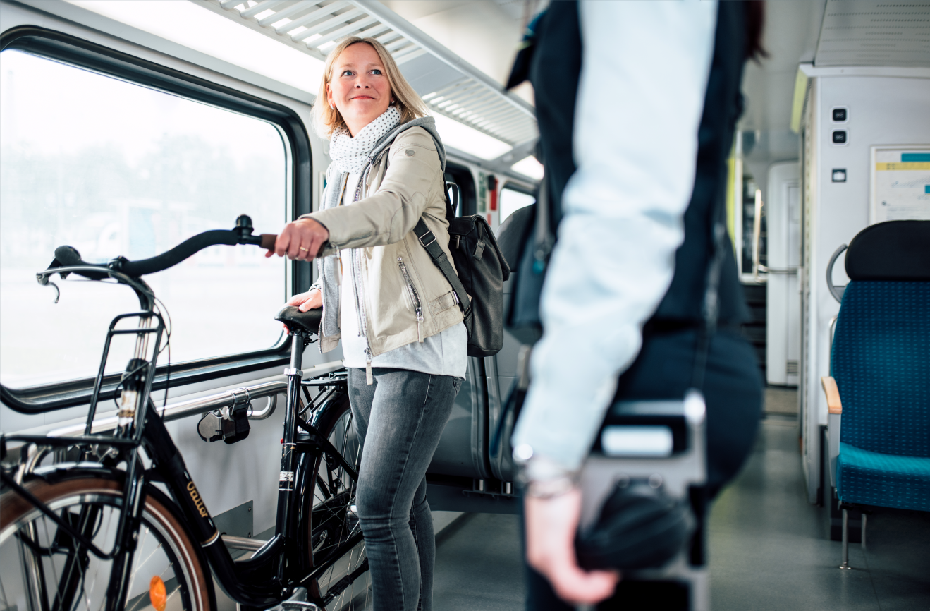 Eine Fahrgästin mit Fahrrad in einem Zug der WestfalenBahn lächelt eine Kundenbetreuerin an.