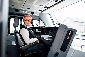 Eine Triebfahrzeugführerin sitzt im Führerstand und lächelt in die Kamera.