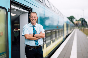 Ein lächelnder Triebfahrzeugführer vor einem Zug der WestfalenBahn.